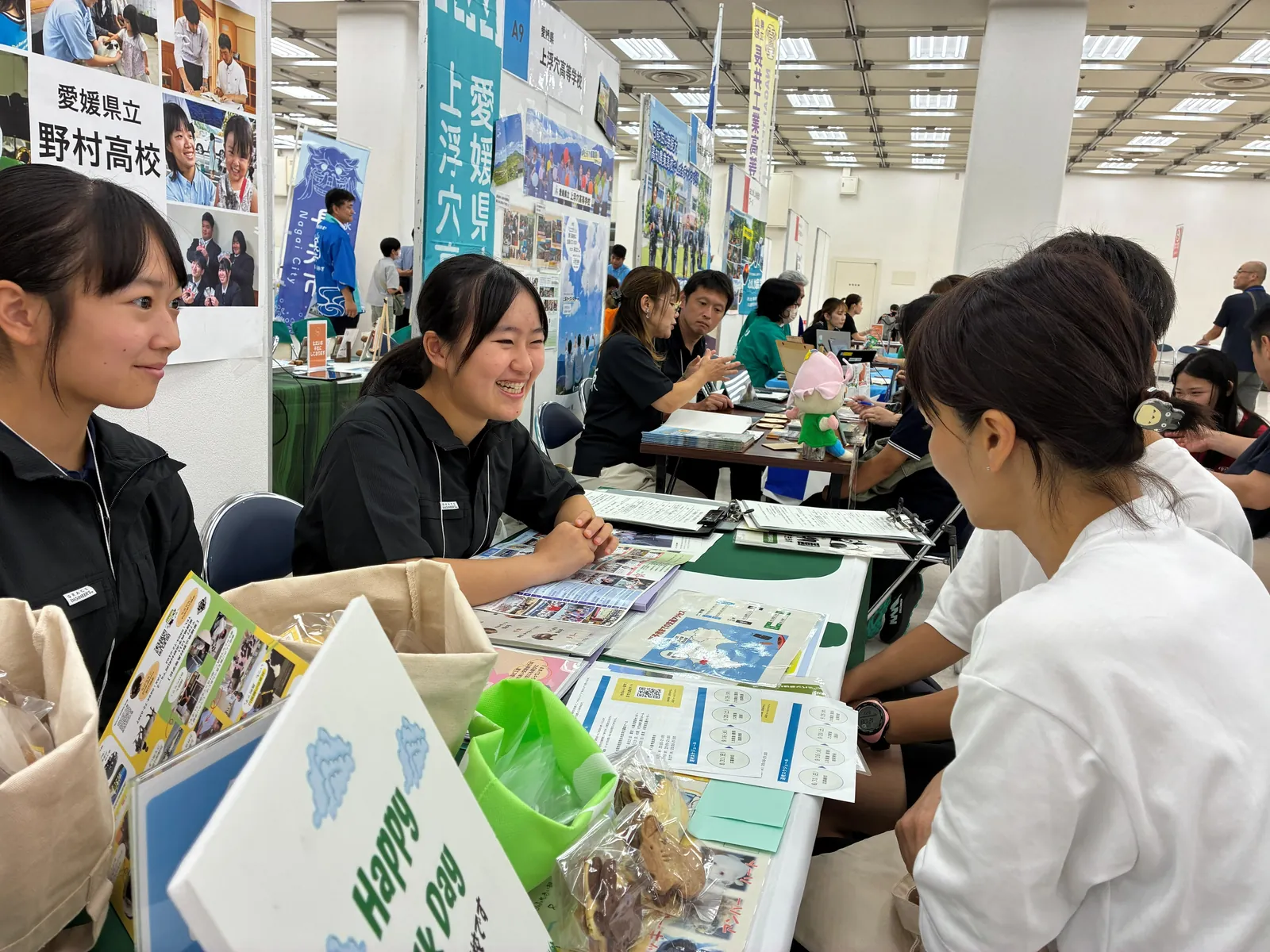 地域みらい留学フェスの会場で、高校のブースにいる生徒と来場者が話している写真