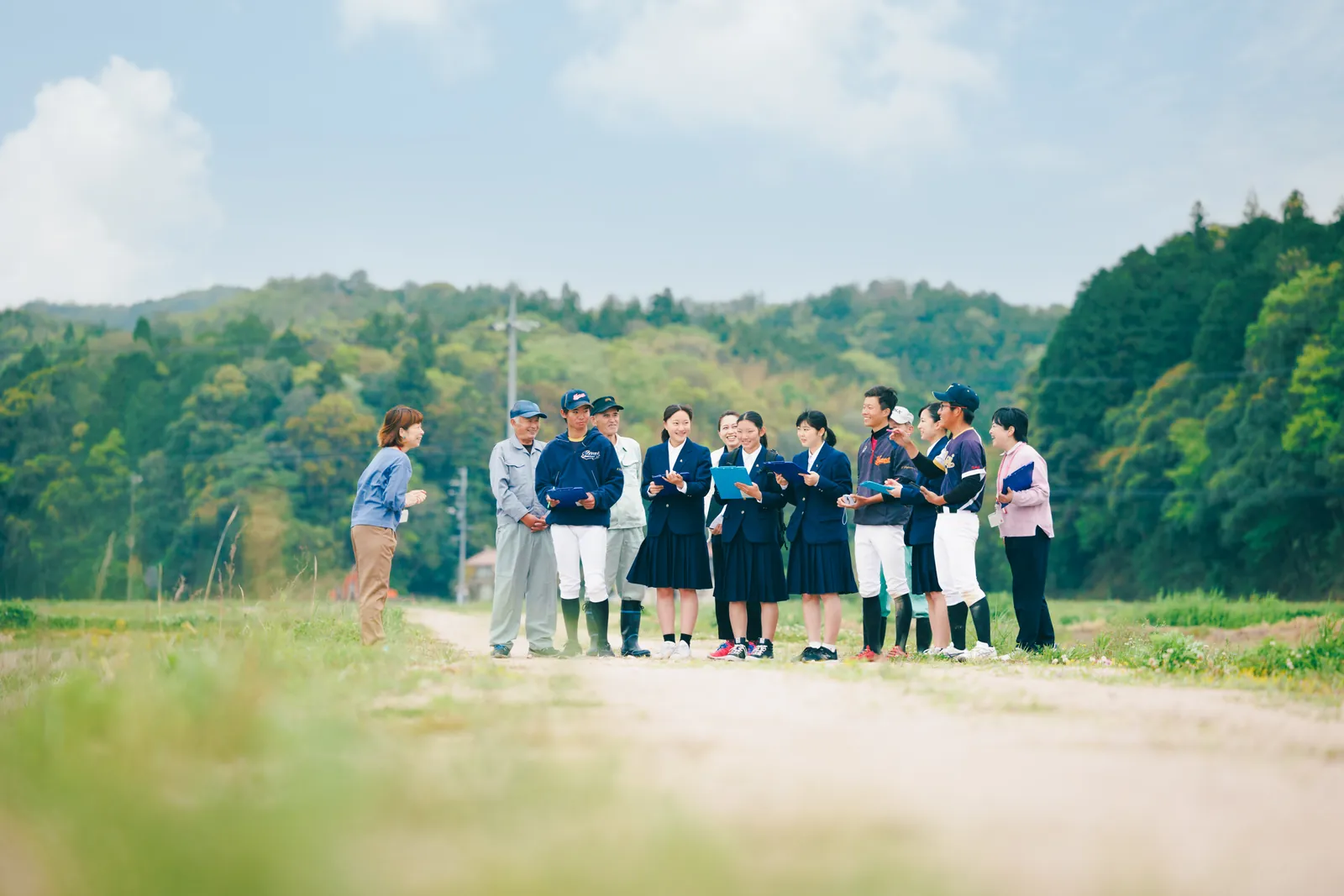 田んぼのそばで、地域の方と生徒たちが話し合っている写真