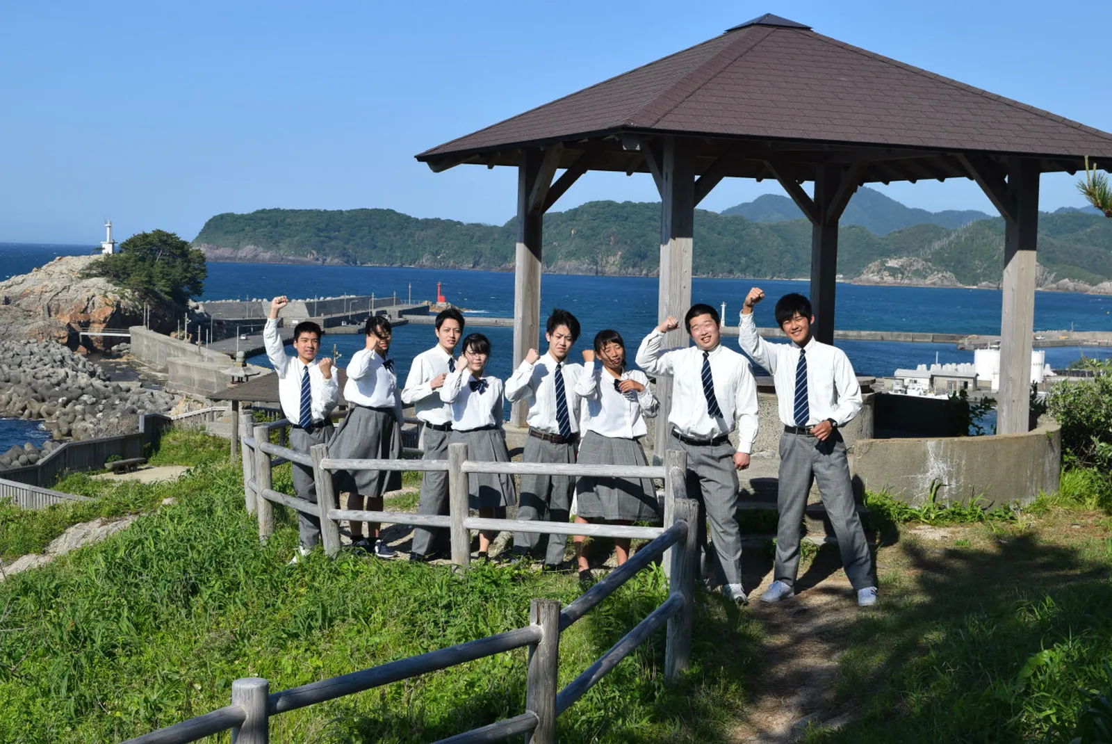 海辺の東屋で高校生たちが元気にポーズを取っている写真