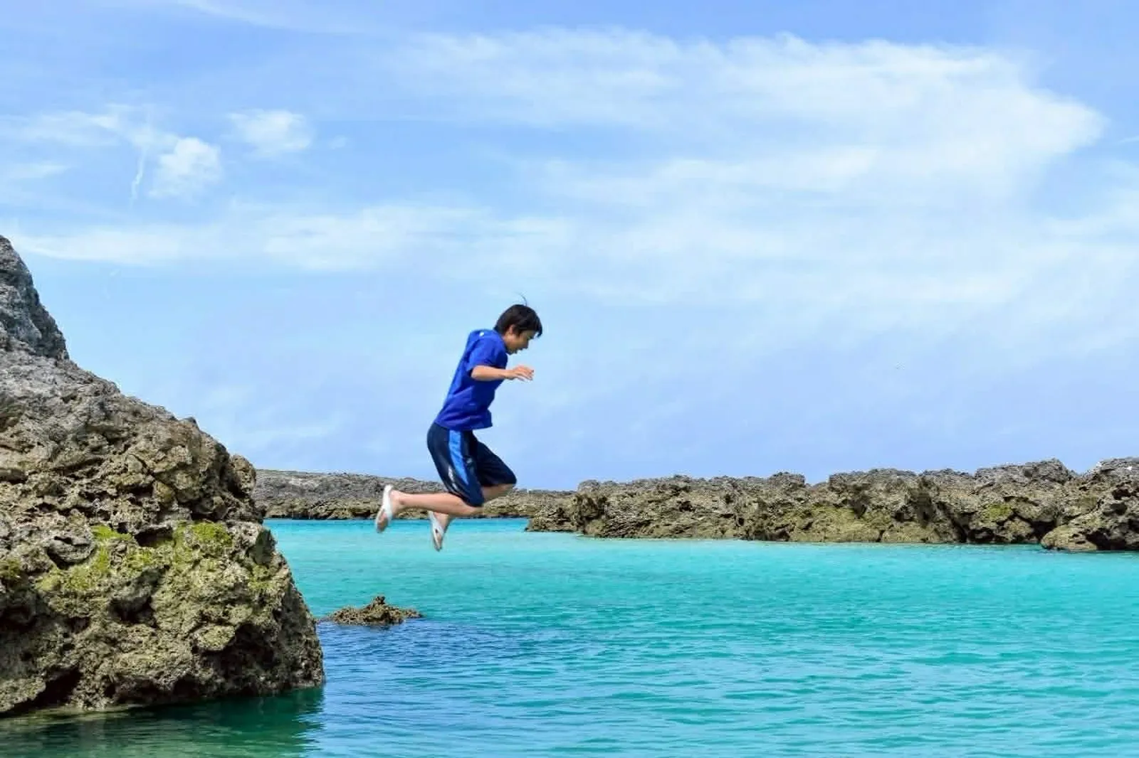 透き通ったターコイズブルーの海に、少年が岩から飛び込んでいる写真